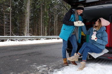 Photo of Couple near open car trunk full of luggage on road, space for text. Winter vacation