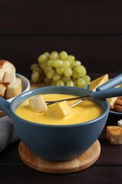 Pot of tasty cheese fondue and forks with bread pieces on wooden table