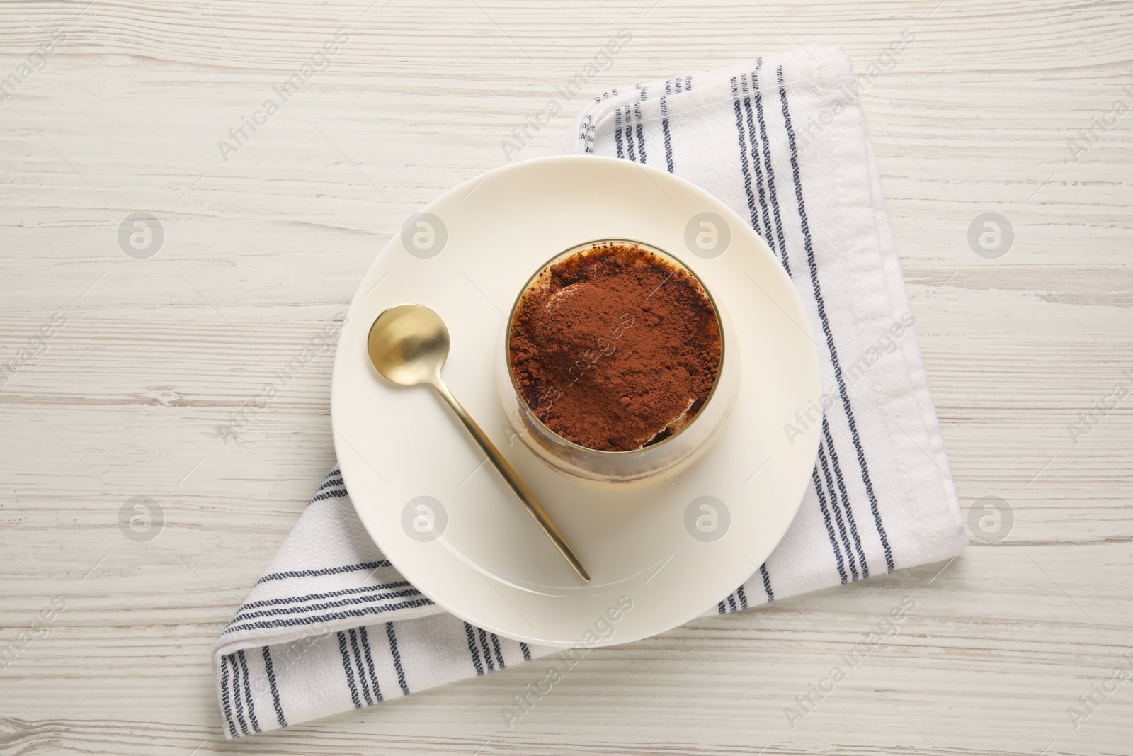 Photo of Delicious tiramisu in glass and spoon on white wooden table, top view