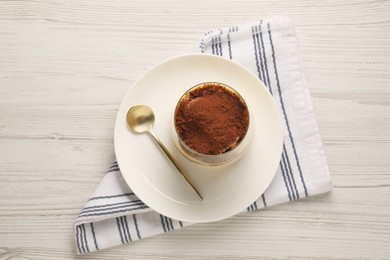 Delicious tiramisu in glass and spoon on white wooden table, top view