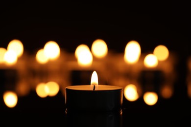 Photo of Burning candle on surface in darkness, closeup