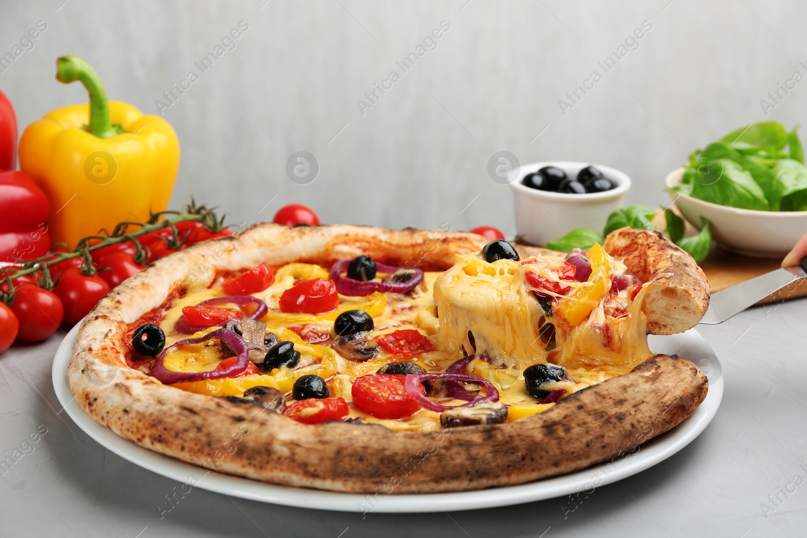 Photo of Taking slice of tasty vegetable pizza with spatula on light grey table, closeup