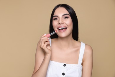 Young woman with beautiful makeup holding nude lipstick on beige background