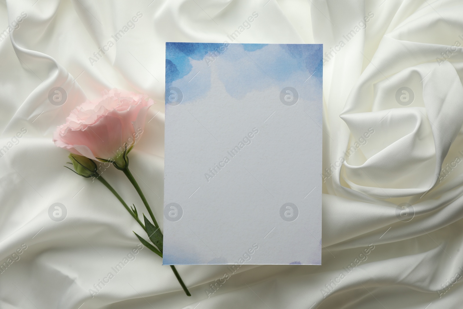 Photo of Blank invitation card and pink flower on white fabric, flat lay