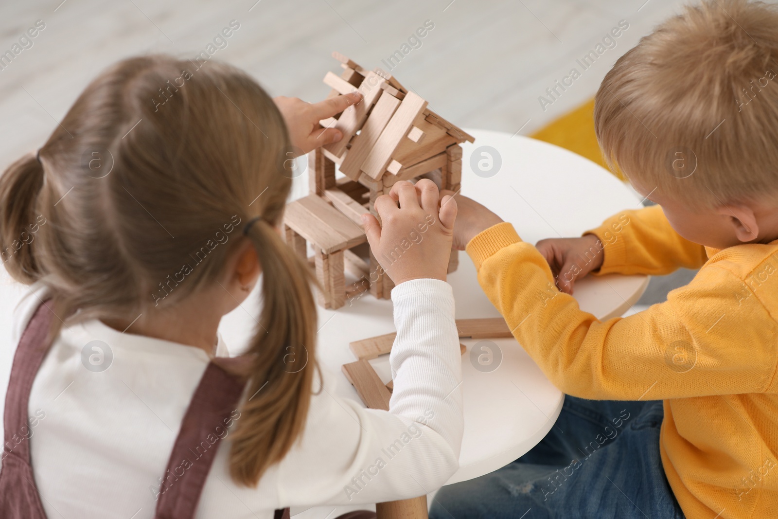 Photo of Little boy and girl playing with wooden house at white table indoors. Children's toys