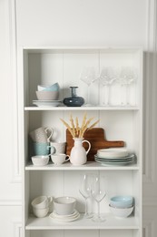 Photo of Different clean dishware and glasses on shelves in cabinet indoors
