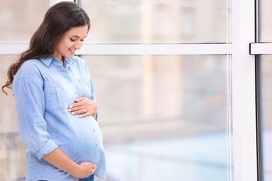 Photo of Beautiful pregnant woman near window at home