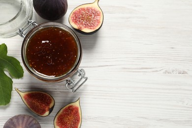 Photo of Glass jar with tasty sweet jam, green leaf and fresh figs on white wooden table, flat lay. Space for text