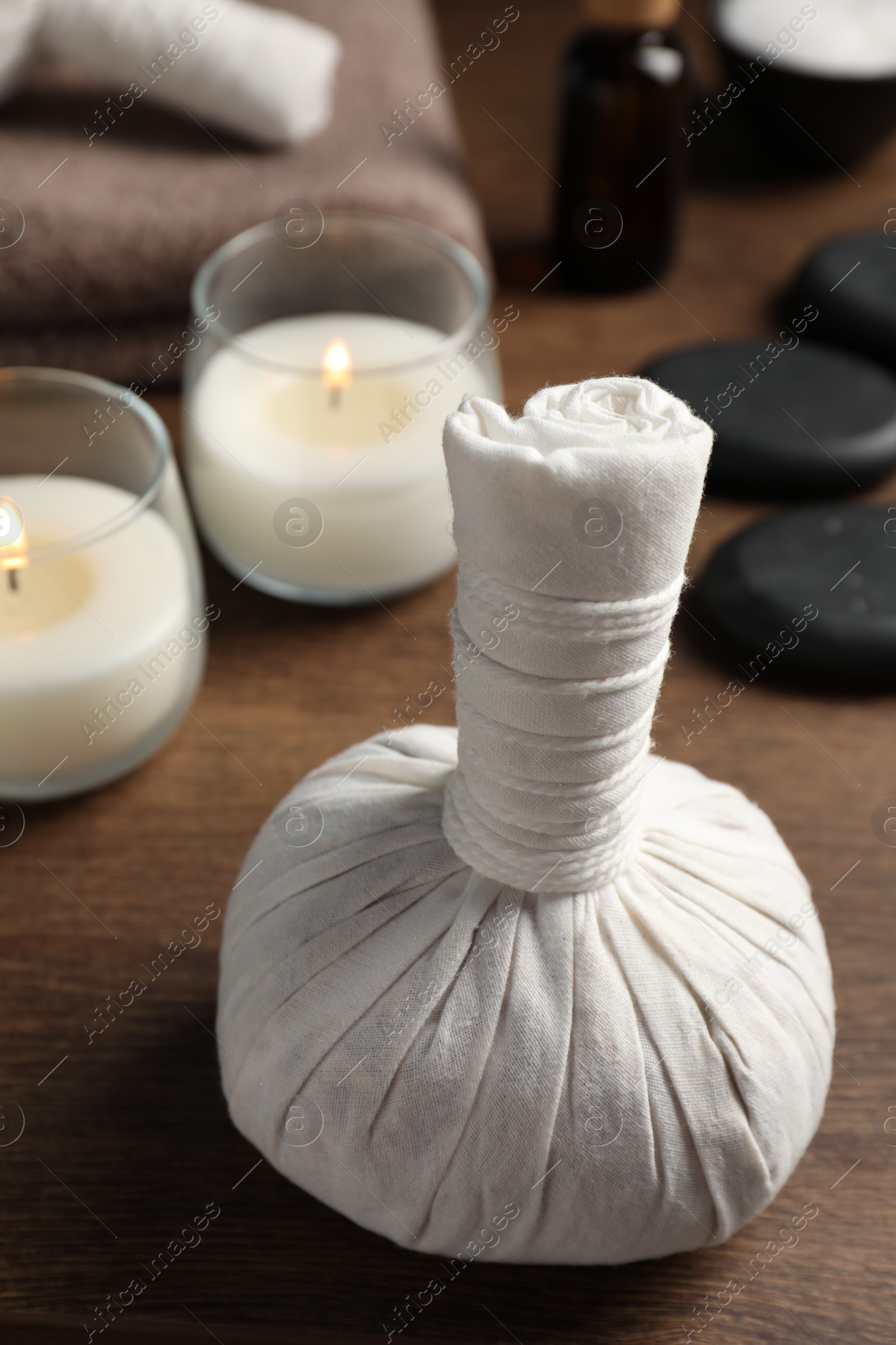 Photo of Herbal massage bag, spa stones and candles on wooden table, closeup