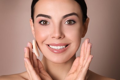 Photo of Beautiful young woman applying face powder with puff applicator on dusty rose background, closeup