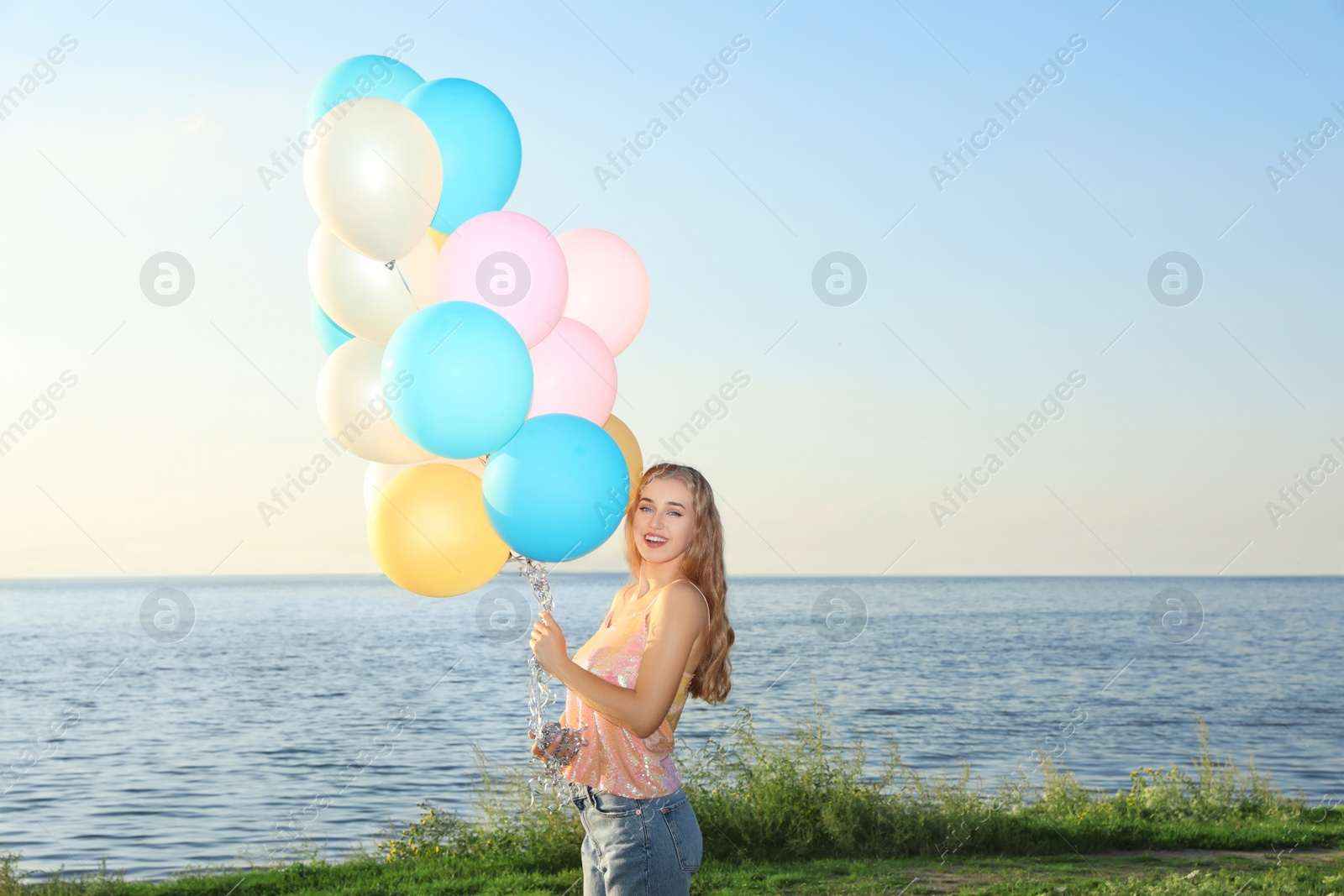 Photo of Beautiful young woman holding colorful balloons on riverside