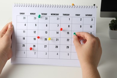 Timetable. Man marking date in calendar with drawing pins at white table, closeup