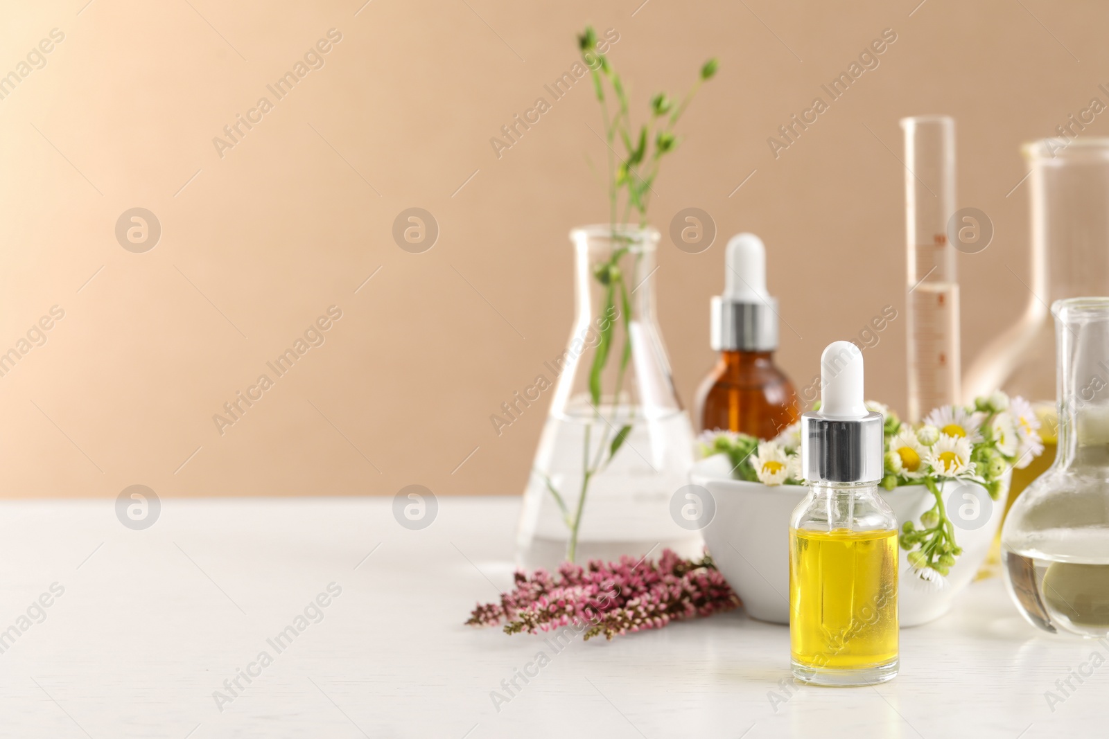 Photo of Cosmetic oil, laboratory dishware and flowers on white table, space for text