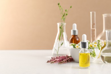 Photo of Cosmetic oil, laboratory dishware and flowers on white table, space for text