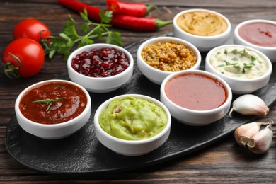 Photo of Different tasty sauces in bowls and ingredients on wooden table, closeup