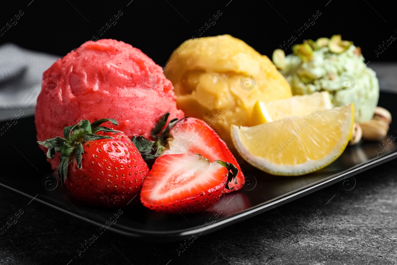 Photo of Strawberry, lemon and pistachio ice cream scoops served on table, closeup