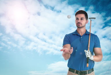 Young man with golf club and ball against blue sky. Space for design