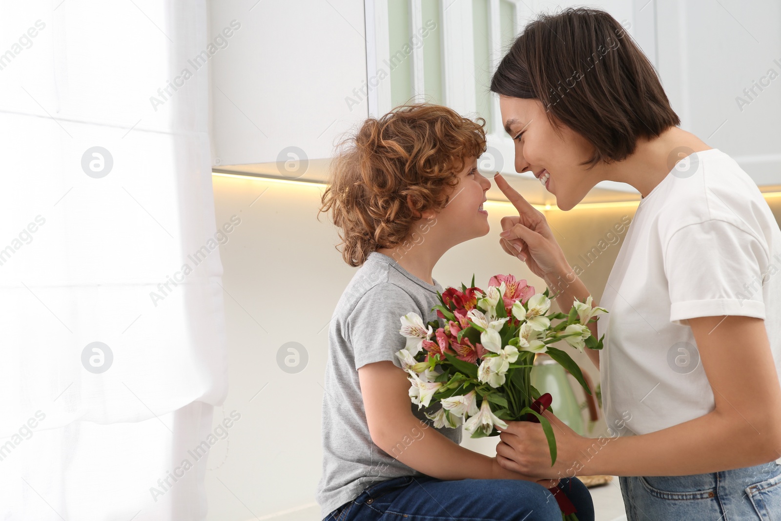 Photo of Happy woman with her cute son and bouquet of beautiful flowers in kitchen, space for text. Mother's day celebration