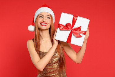 Photo of Young woman in Santa hat with Christmas gift on red background