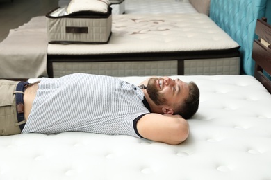 Photo of Smiling man lying on orthopedic mattress in store