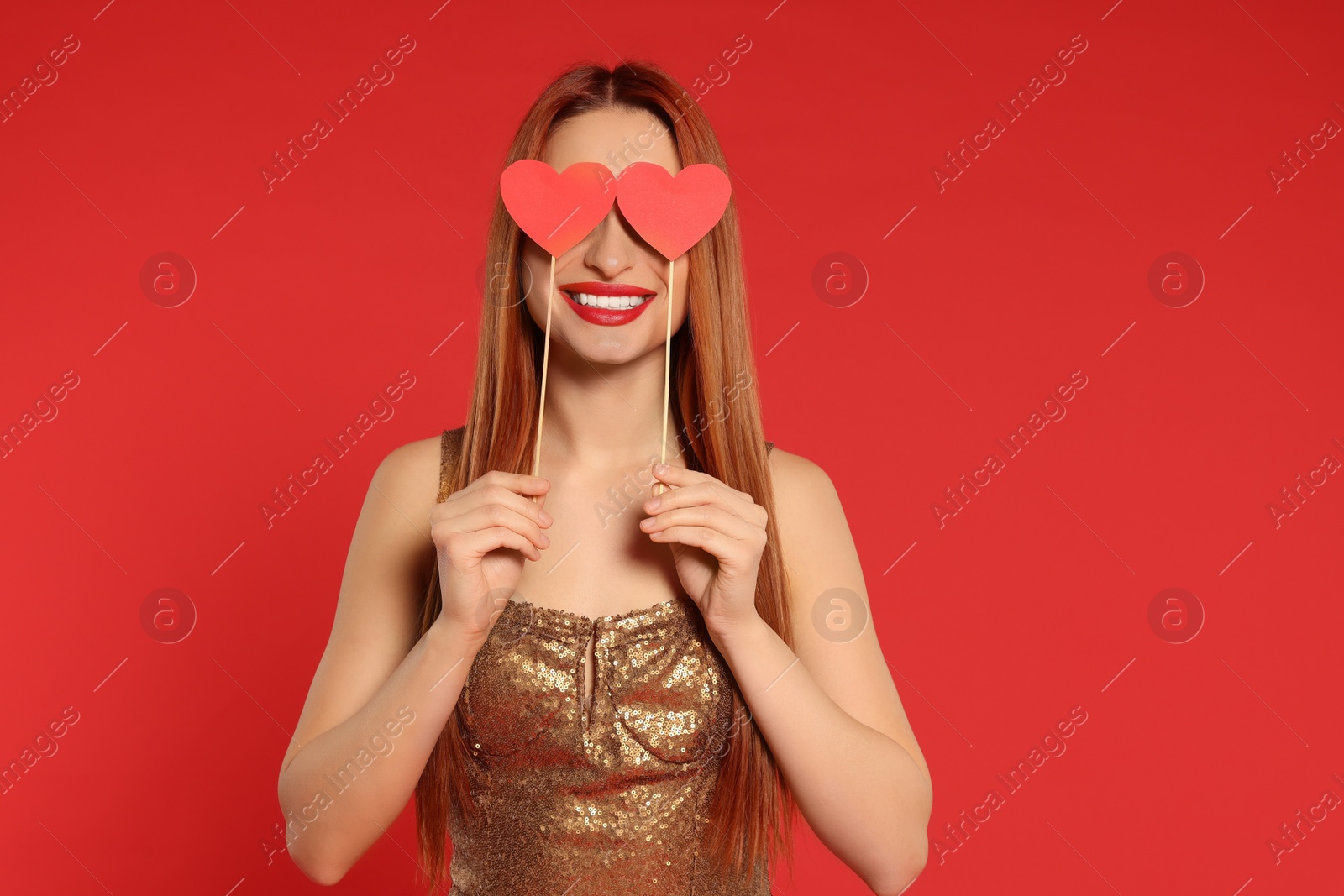 Photo of Young woman in dress covering her eyes with paper hearts on red background