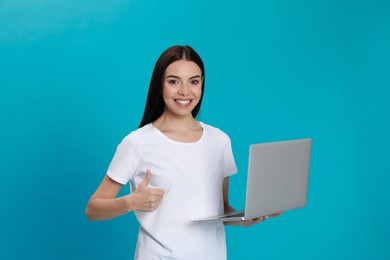 Young woman with modern laptop on light blue background