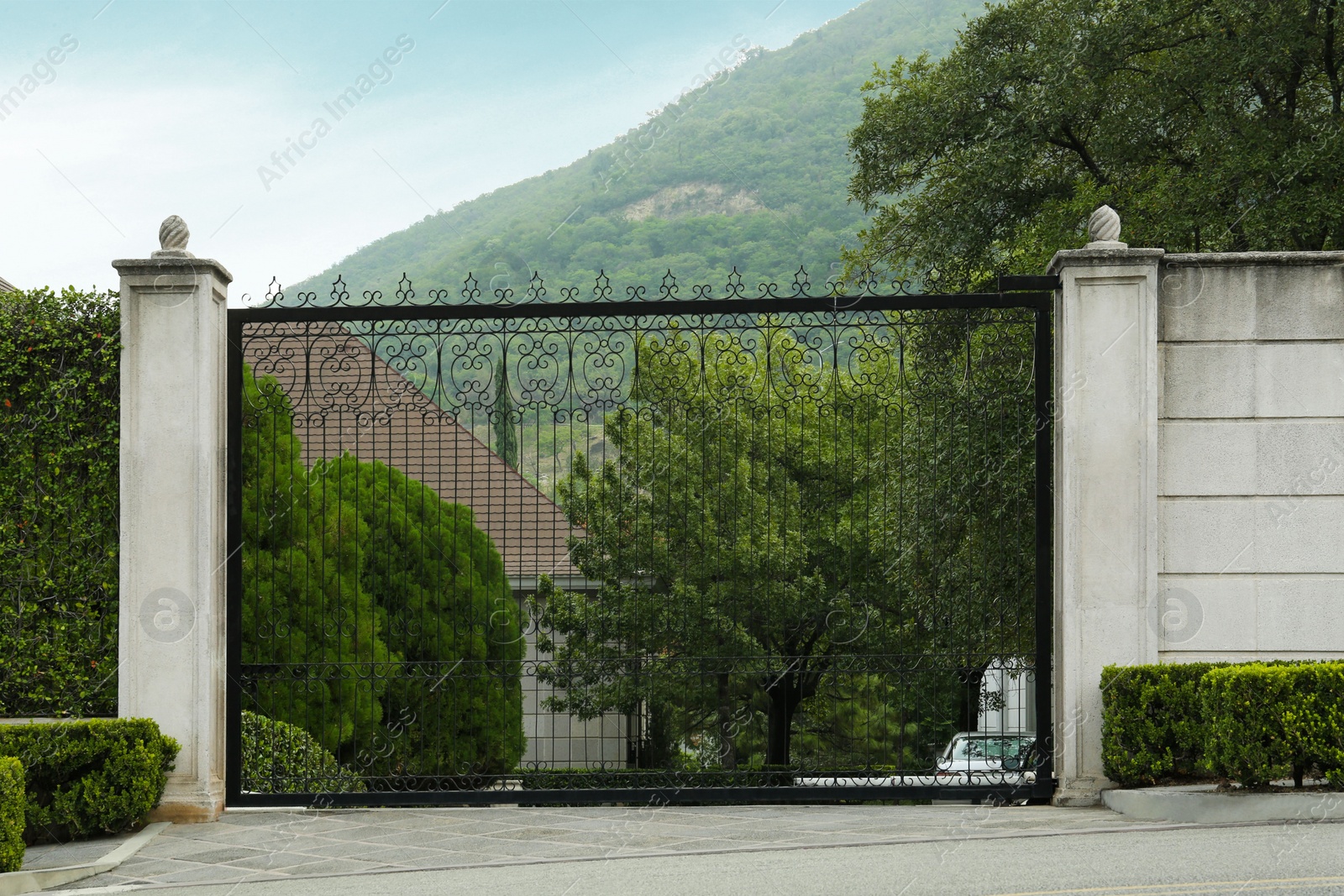 Photo of Beautiful stone fence with ornate black metal gates around house and garden