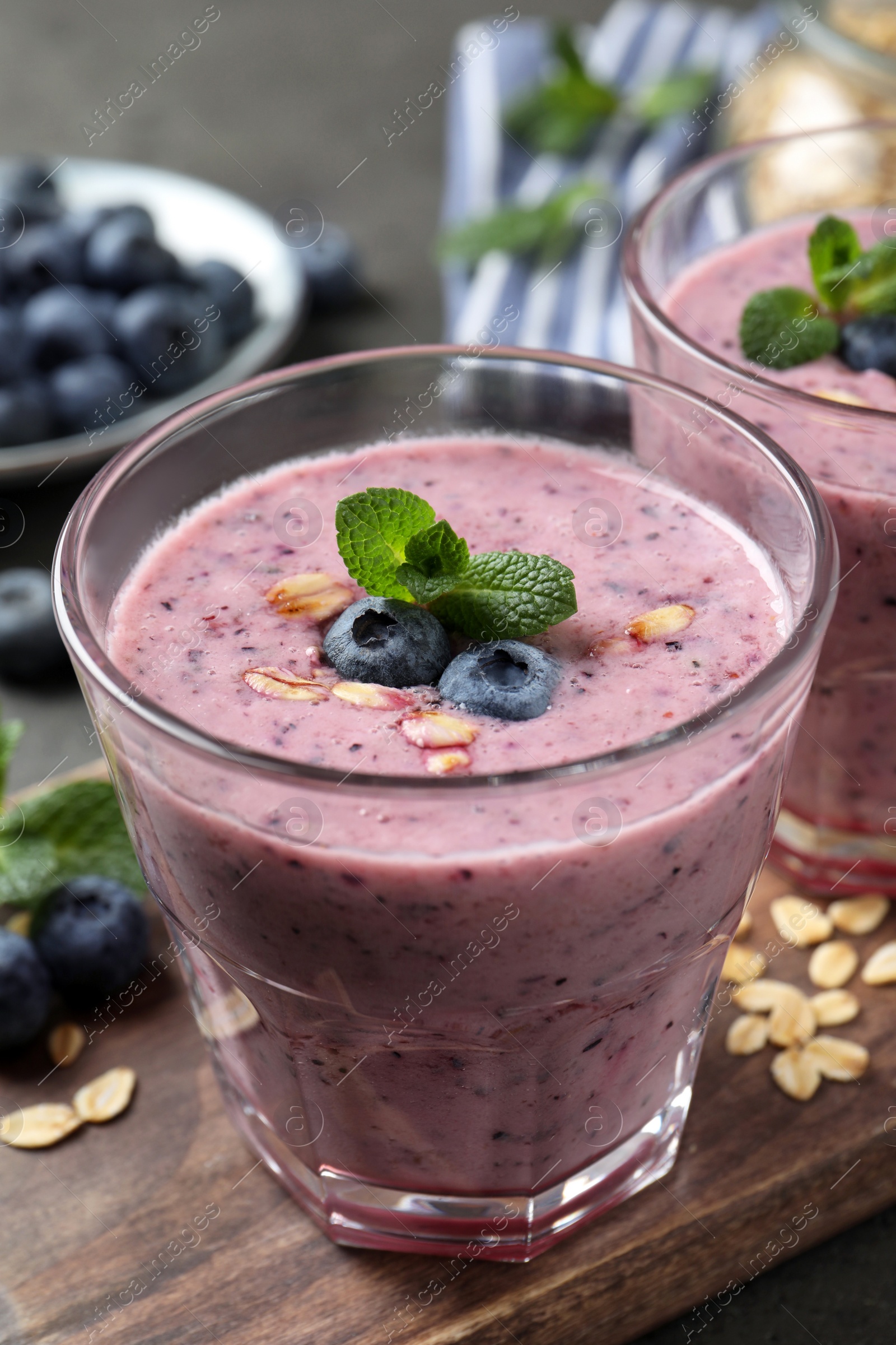 Photo of Glass of tasty blueberry smoothie with oatmeal on wooden board, closeup