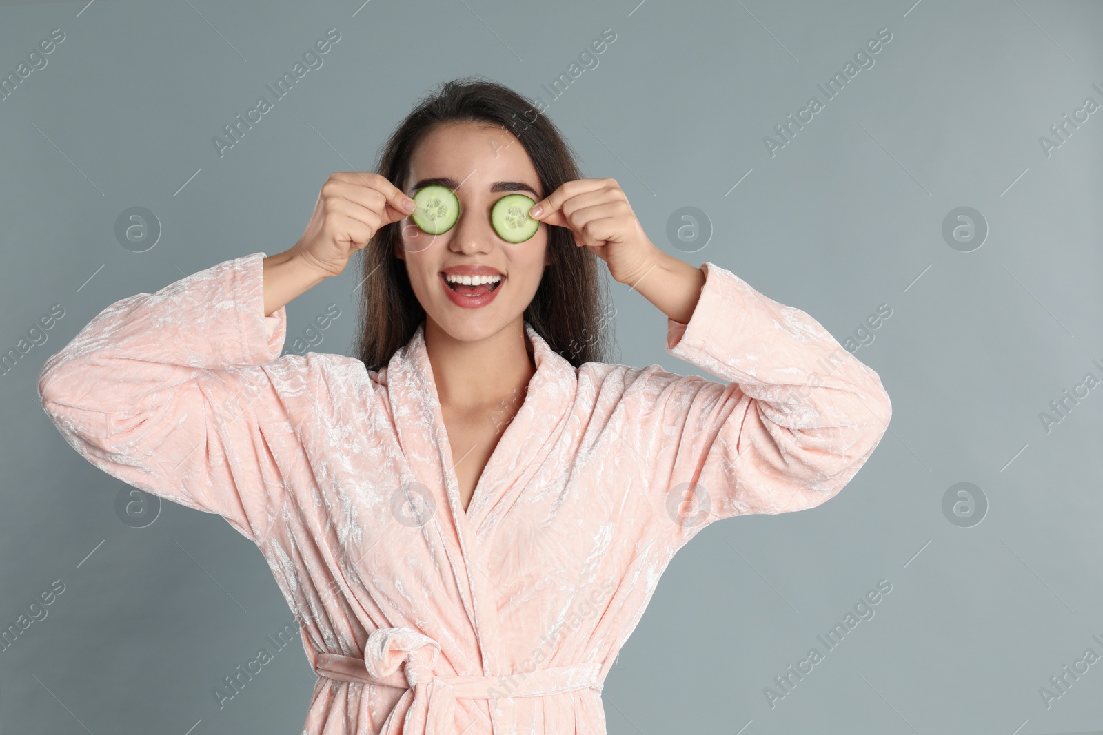 Photo of Young woman in bathrobe with cucumber slices on grey background