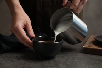 Photo of Woman pouring milk into cup of coffee at grey table, closeup