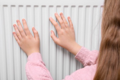 Photo of Girl warming hands on heating radiator, closeup