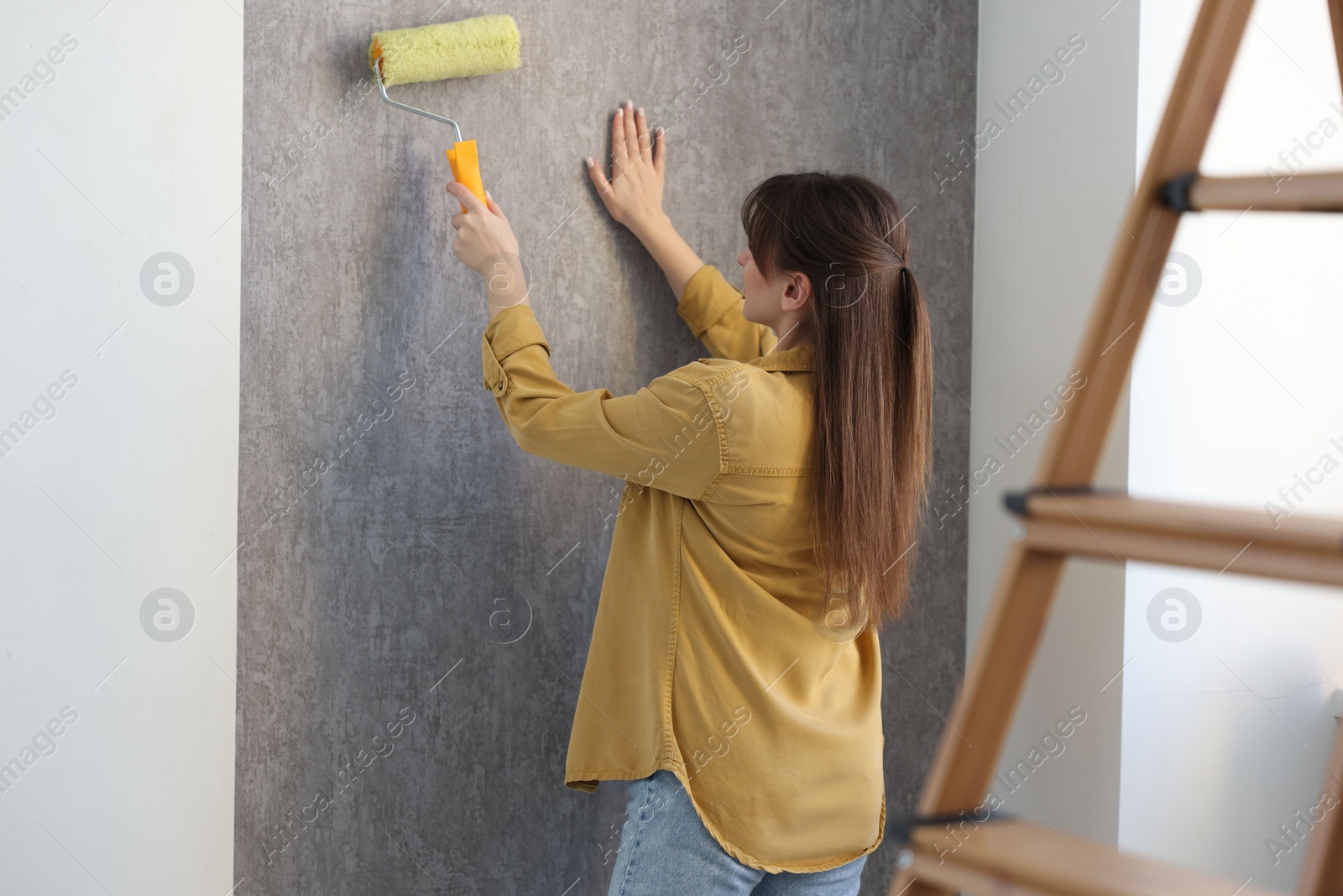 Photo of Woman hanging stylish gray wallpaper in room