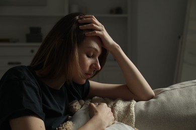 Photo of Sad young woman sitting on sofa at home