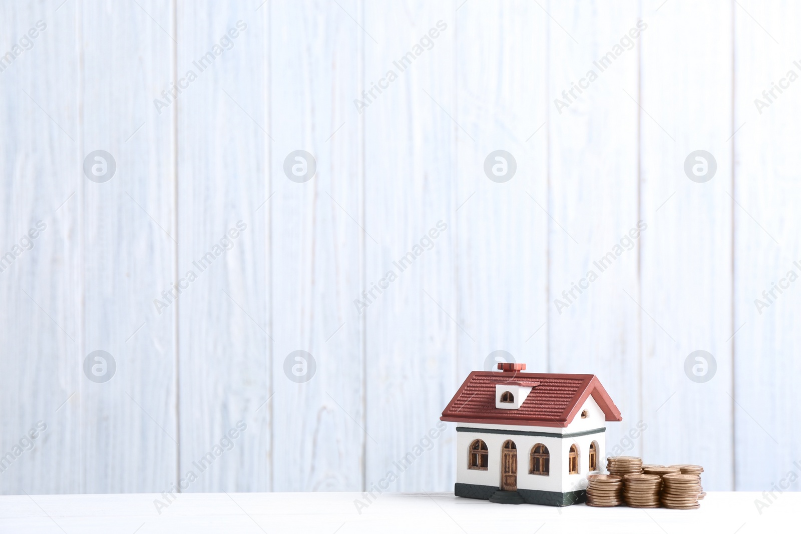 Photo of House model and coins on table against wooden background. Space for text