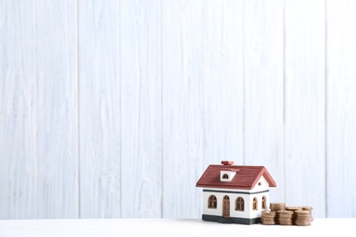 House model and coins on table against wooden background. Space for text