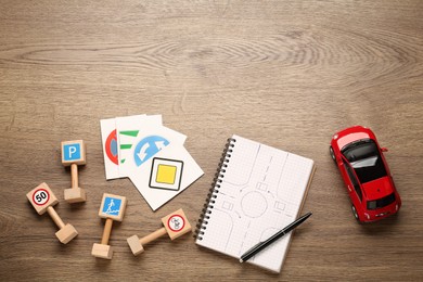 Photo of Many different road signs, notebook and toy car on wooden background, flat lay with space for text. Driving school