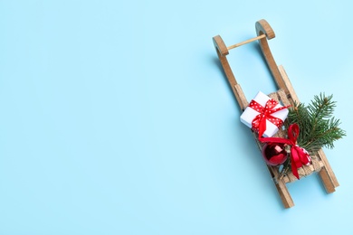 Photo of Sleigh with gift box and fir tree branch on light blue background, top view. Space for text