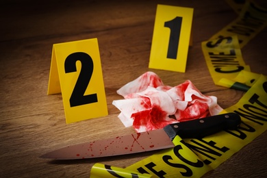 Photo of Knife, bloody napkin and crime scene markers on wooden table