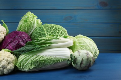 Photo of Many different fresh cabbages on blue wooden table