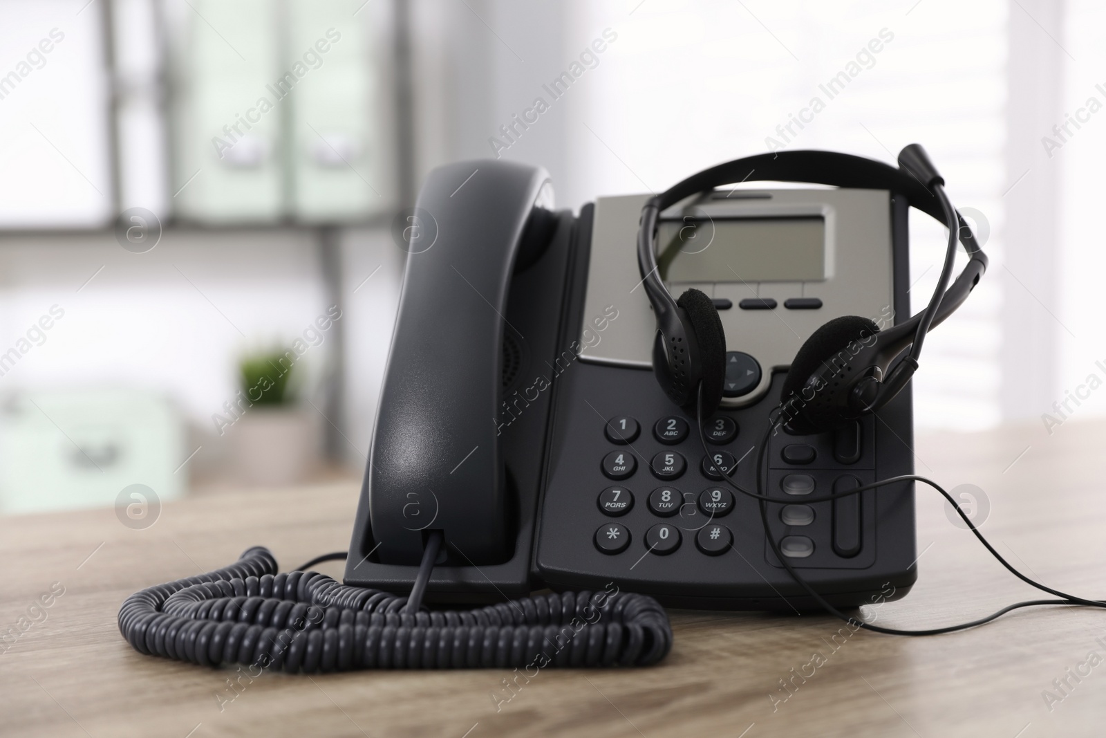 Photo of Desktop telephone and headset on wooden table in office. Hotline service