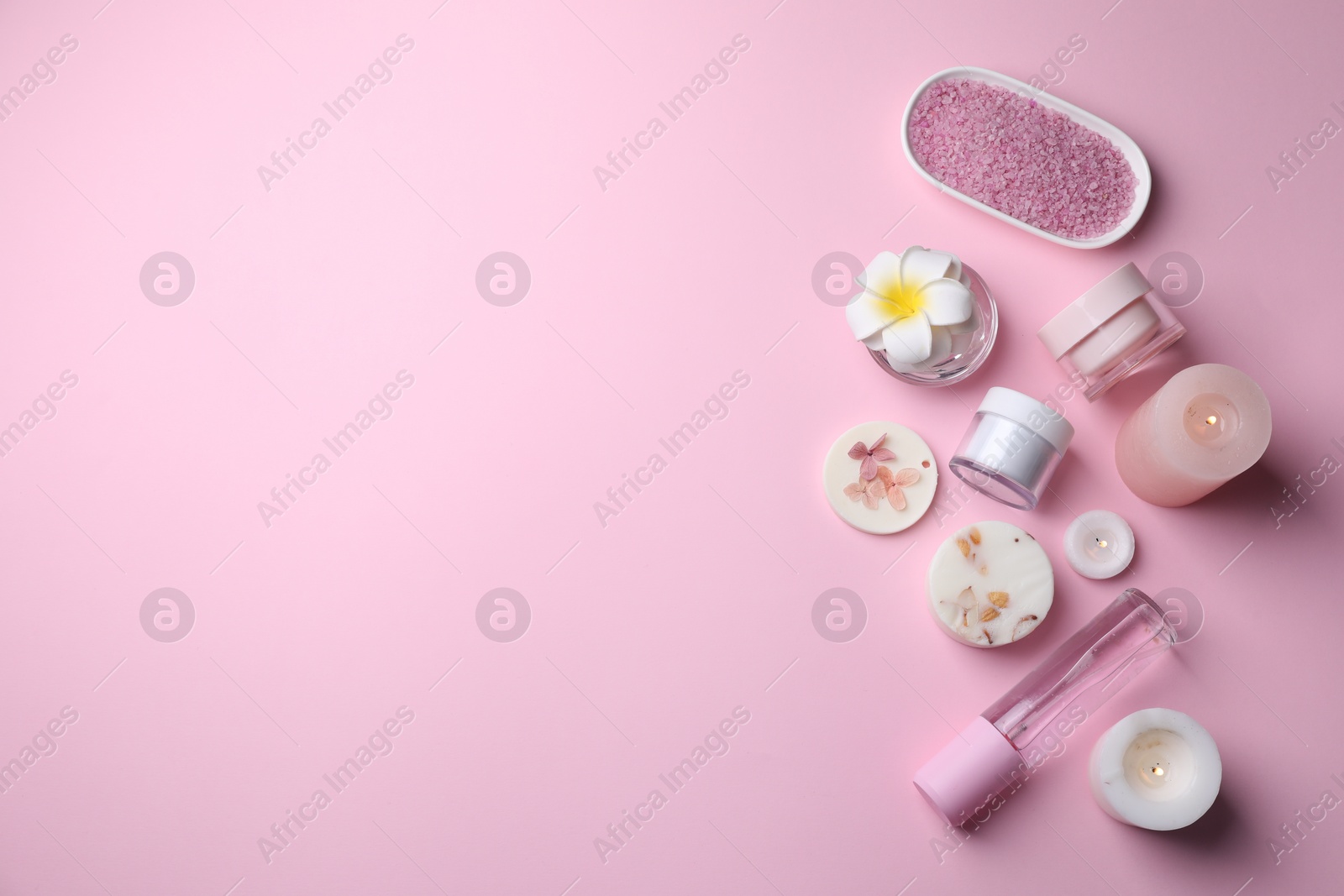 Photo of Different spa products, plumeria flower and burning candles on pink background, flat lay. Space for text