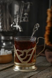 Photo of Glass of tea in vintage holder and samovar on wooden table