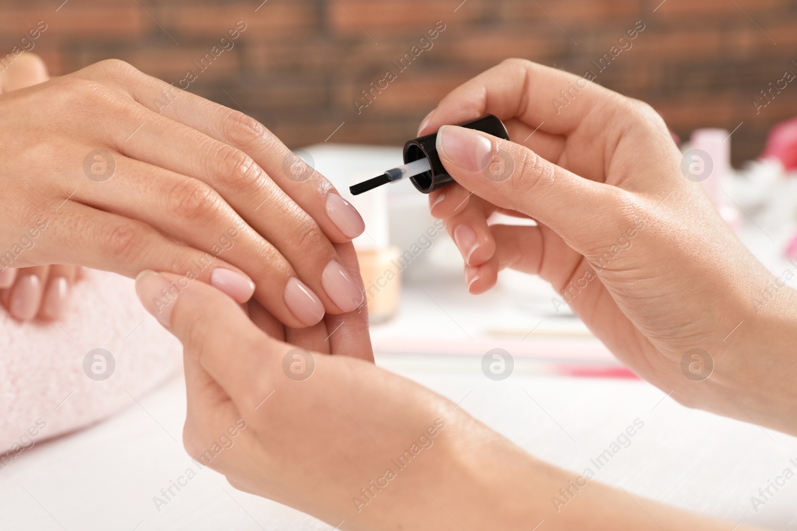 Photo of Manicurist applying polish on client's nails at table, closeup. Spa treatment