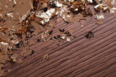 Photo of Many pieces of edible gold leaf on wooden table, top view. Space for text