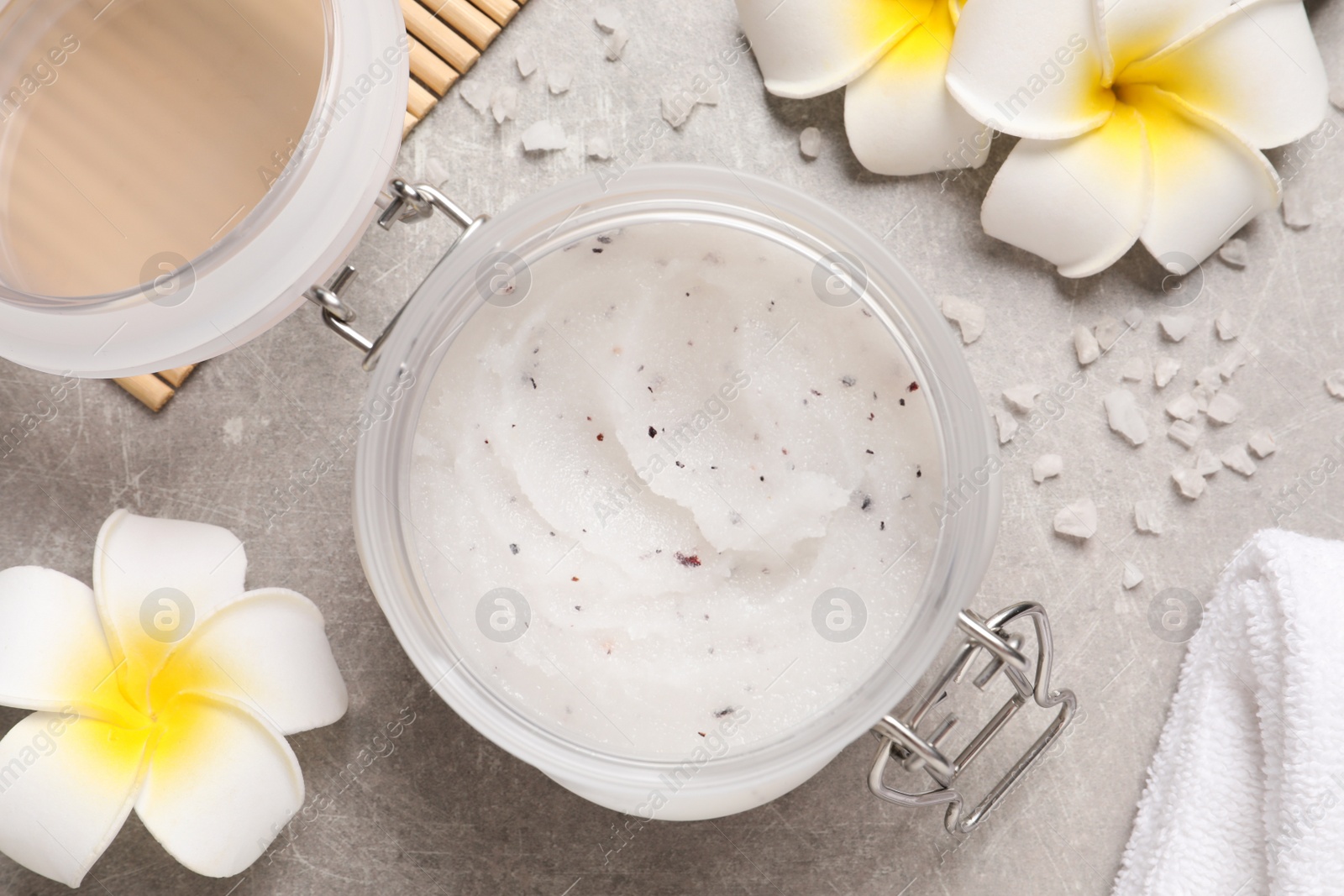 Photo of Body scrub, sea salt and plumeria flowers on grey table, flat lay