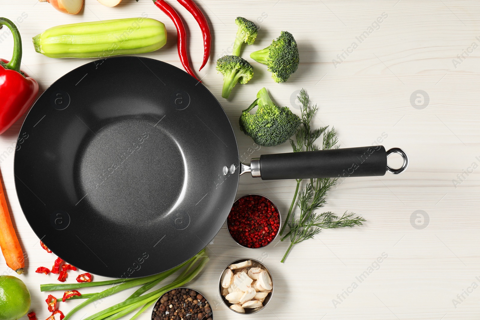 Photo of Empty iron wok surrounded by raw ingredients on white wooden table, flat lay