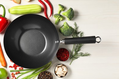 Empty iron wok surrounded by raw ingredients on white wooden table, flat lay