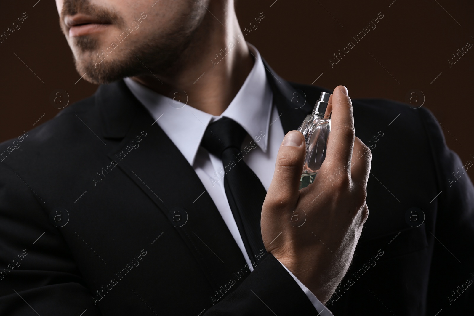 Photo of Handsome man in suit using perfume on dark background, closeup