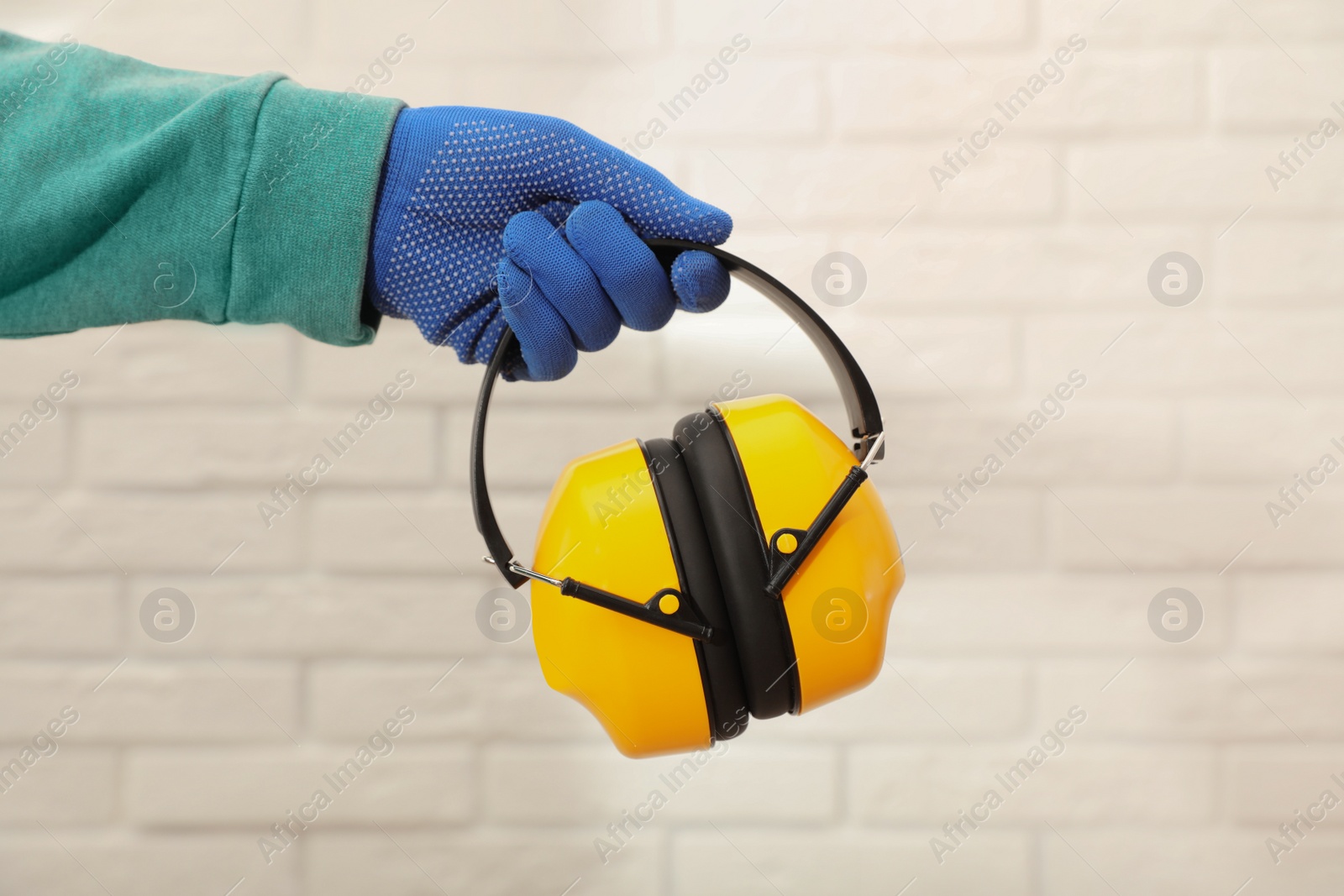 Photo of Worker holding safety headphones against white brick wall, closeup. Hearing protection device