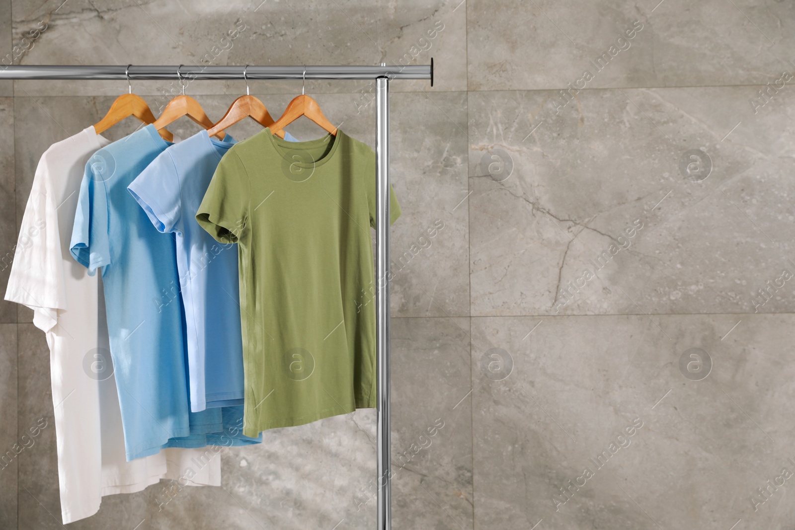 Photo of Clean T-shirts hanging on rack near gray marble wall. Space for text